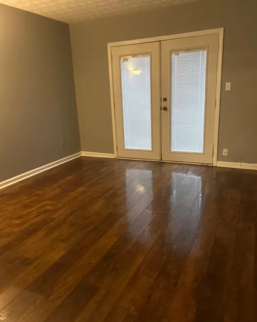 Empty room with dark hardwood floors reflecting light from french doors